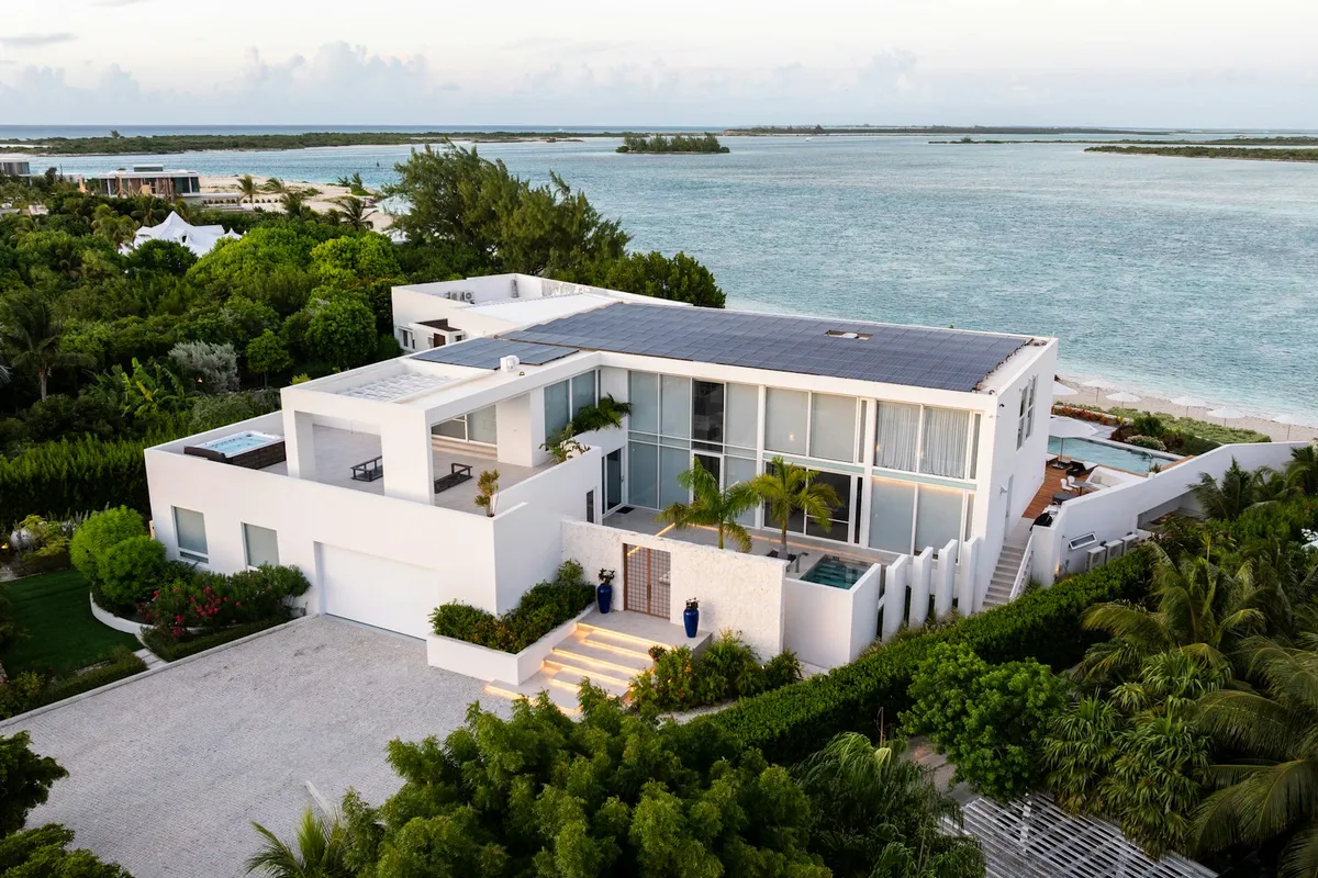 Vista aérea de una residencia blanca de concreto con paneles solares frente al mar